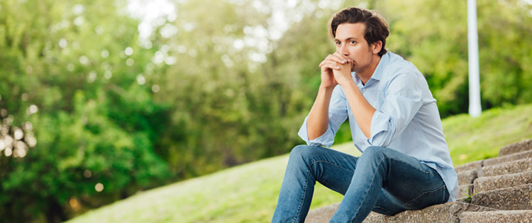 man sitting outside thinking with head resting on hands