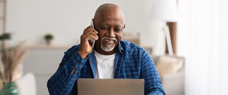 An older man talking on the phone and looking at a laptop.