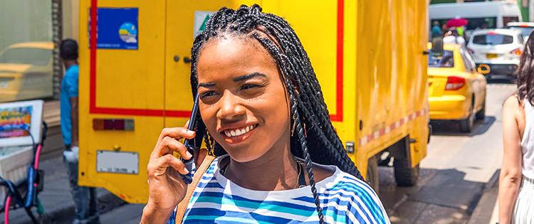 Una mujer con trenzas hablando por teléfono por la calle con un camión amarillo detrás.
