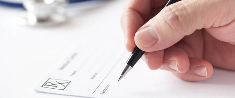 Photo of a doctor's hand writing on a prescription pad.