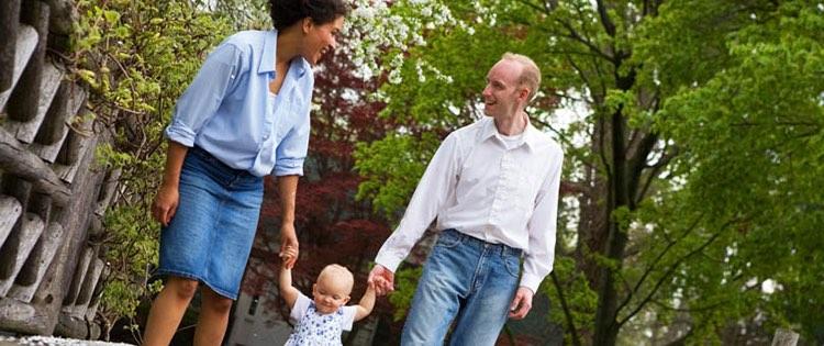 Photo of an interracial couple walking and holding hands with their baby.