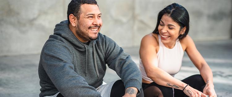 A man and a woman in workout clothes sitting together and smiling. 