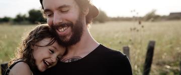 In a field, a smiling man embracing a young smiling girl.