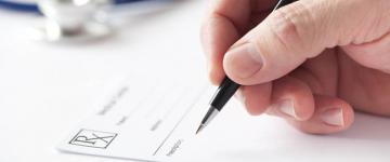 Photo of a doctor's hand writing on a prescription pad.