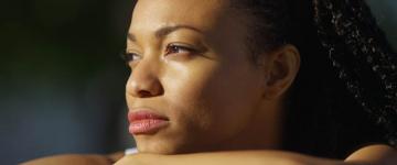 Photo of a young Black woman thinking and looking toward sunlight