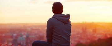 Young man turned away from camera gazing at sunset over city