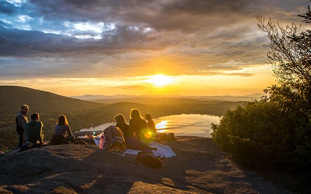 A group of friends enjoy the sunrise after climbing a mountain together.  