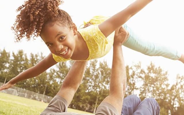 Adult lying on ground and holding smiling child up in the air