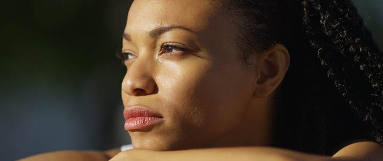 Photo of a young Black woman thinking and looking toward sunlight